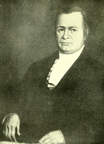 Portrait of Jones. He is wearing a scarf and jacket. He has longer hair that is pulled back, a cleft chin, and he has a stern expression.